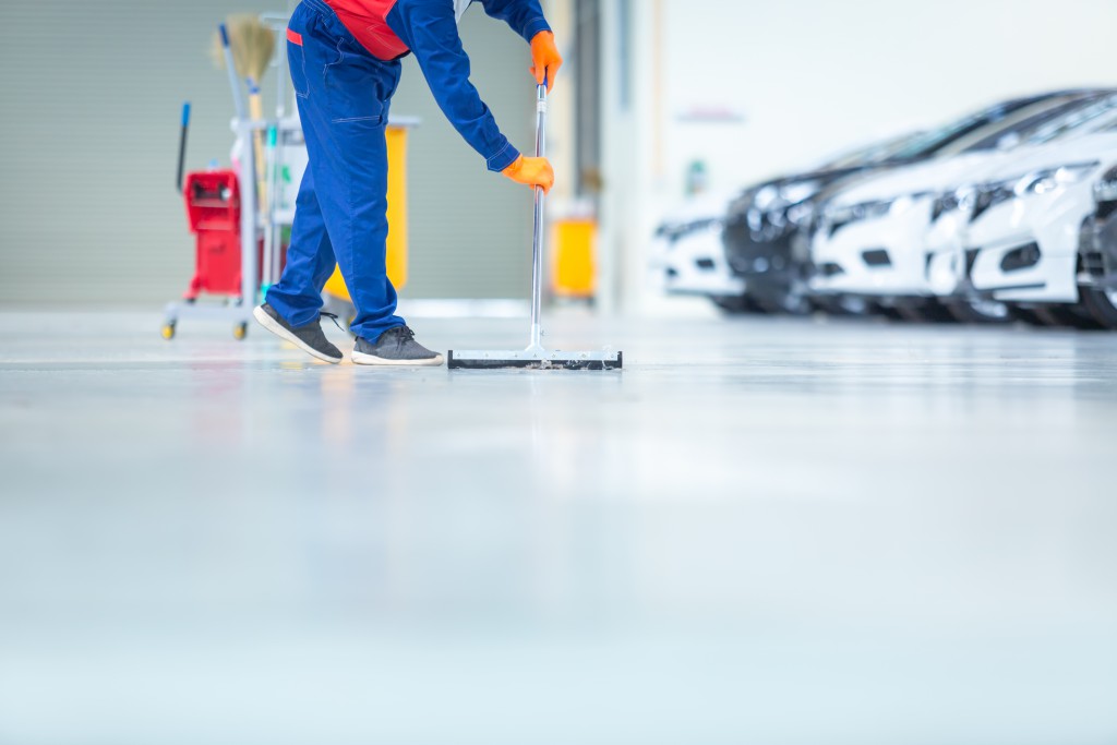 Car mechanic repair service center cleaning using mops to roll w Car mechanic repair service center cleaning using mops to roll water from the epoxy floor. In the car repair service center.