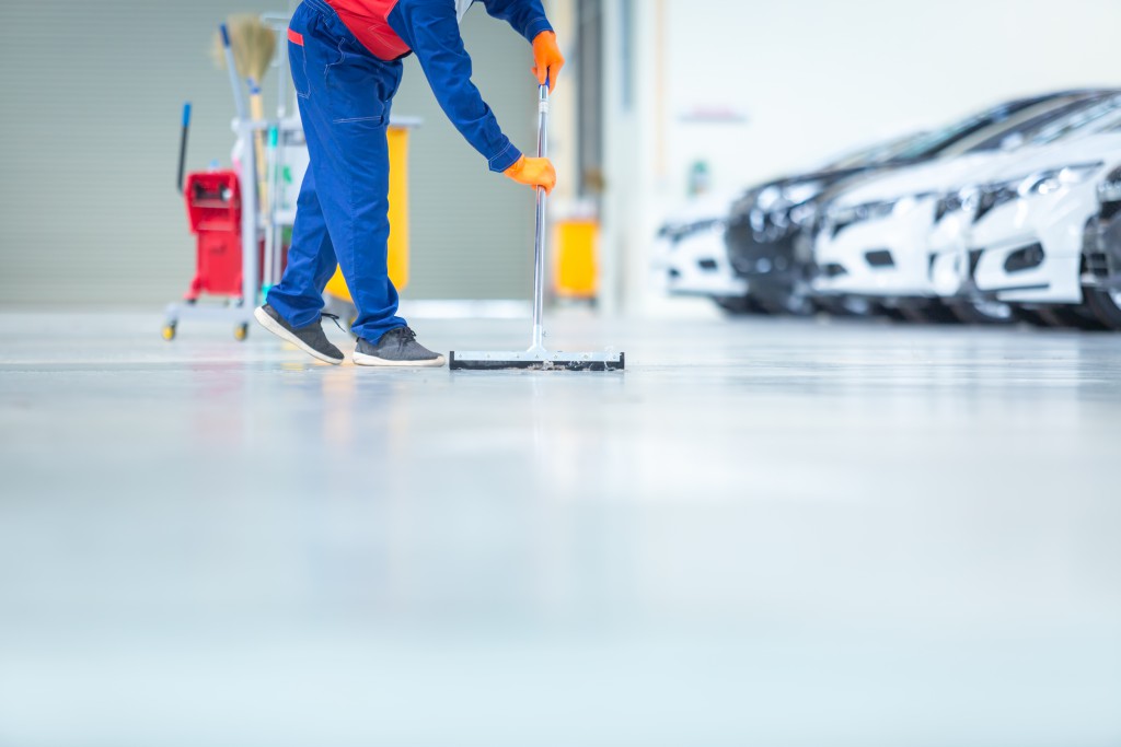 Car mechanic repair service center cleaning using mops to roll water from the epoxy floor. In the car repair service center.